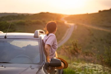 Arabasında yaz şapkası olan bir kadın yolda seyahat ediyor. Özgürlük, seyahat ve tatil yolculuğu konsept yaşam tarzı imajı