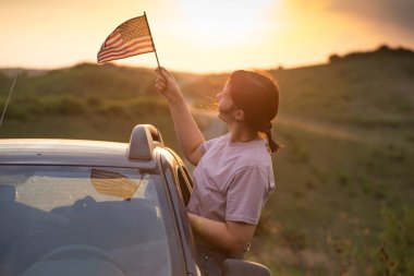 Gün batımında Amerikan bayrağı taşıyan bir kadın. Bağımsızlık Günü ya da Amerika 'da seyahat.