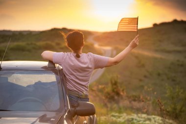 Gün batımında Amerikan bayrağı taşıyan bir kadın. Bağımsızlık Günü ya da Amerika 'da seyahat.