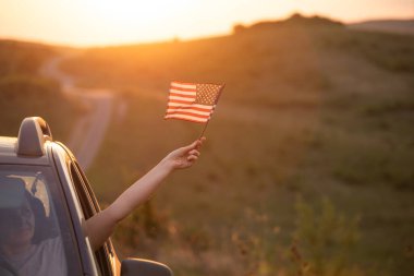 Gün batımında Amerikan bayrağı taşıyan bir kadın. Bağımsızlık Günü ya da Amerika 'da seyahat.