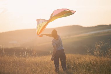 Sihirli günbatımında elinde Gay Gökkuşağı Bayrağı tutan bir kadın. Aynı cinsiyet çiftleri için mutluluk, özgürlük ve aşk kavramı
