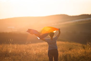 Sihirli günbatımında elinde Gay Gökkuşağı Bayrağı tutan bir kadın. Aynı cinsiyet çiftleri için mutluluk, özgürlük ve aşk kavramı