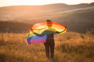 Sihirli günbatımında elinde Gay Gökkuşağı Bayrağı tutan bir kadın. Aynı cinsiyet çiftleri için mutluluk, özgürlük ve aşk kavramı