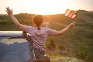 Gün batımında Amerikan bayrağı taşıyan bir kadın. Bağımsızlık Günü ya da Amerika 'da seyahat.