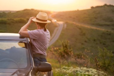 Arabasında yaz şapkası olan bir kadın yolda seyahat ediyor. Özgürlük, seyahat ve tatil yolculuğu konsept yaşam tarzı imajı