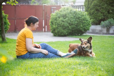 Neşeli, mutlu genç bir kadın yazın evin bahçesinde köpeğiyle oynuyor.. 