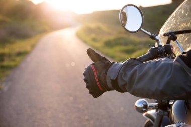 Gün batımında yolda motosiklet sürücüsü OK işareti gösteriyor. Seyahat ve spor, hız ve özgürlük kavramı