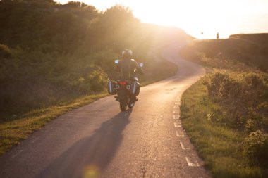 Gün batımında yolda motosiklet sürücüsü. Seyahat ve spor, hız ve özgürlük kavramı