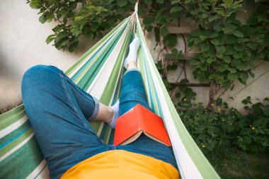 Hamakta kitap okuyan bir kadın. Yavaş yaşam kavramı, şehir koşuşturmasından neşeli bir kaçış.