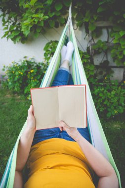 Hamakta kitap okuyan bir kadın. Yavaş yaşam kavramı, şehir koşuşturmasından neşeli bir kaçış.