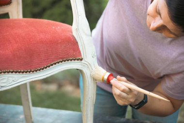 Evdeki klasik bir koltuğu boyayan orta yaşlı kadın, taşınma ve diy konsepti..