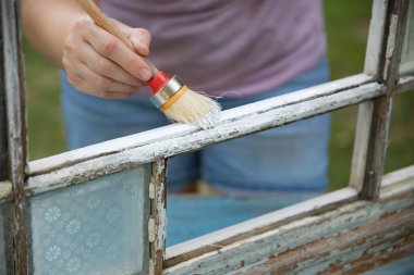 Evdeki klasik bir pencereyi boyayan orta yaşlı kadın, taşınma ve diy konsepti..