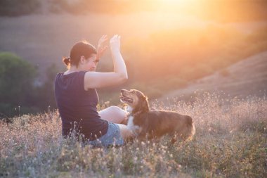 Rahatlamış kadın ve köpek tepenin üstünde yaz günbatımının tadını çıkarıyorlar..