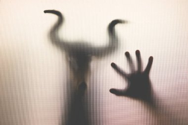 Karanlıkta, pencerenin arkasında boynuzları olan ürkütücü bir kafatası figürü