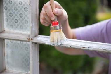 Evdeki klasik bir pencereyi boyayan orta yaşlı kadın, taşınma ve diy konsepti..