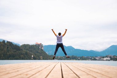 Kolları havada mutlu bir kadın Slovenya 'da Bled Gölü' nün tahta iskelesinde zıplıyor..
