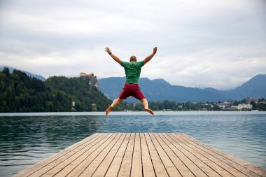Kolları havada mutlu bir adam Slovenya 'da Bled Gölü' nün tahta iskelesinde zıplıyor..