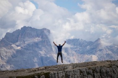 Dolomitlerle dağın tepesine atlayan mutlu bir adam. Spor ve seyahat yaşam tarzı konsepti