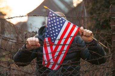 Amerikan Bayrağı 'nı ABD sınırında dikenli tellerin yanında tutan adam. Amerikan göçmenlik ve ABD mülteci krizi kavramı