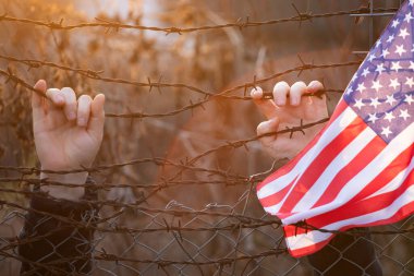 Amerikan bayrağı, ABD sınırındaki dikenli tellere bağlı. Amerikan göçmenlik ve ABD mülteci krizi kavramı
