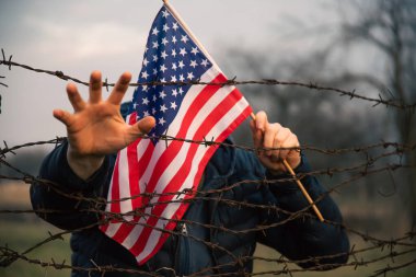 Amerikan Bayrağı 'nı ABD sınırında dikenli tellerin yanında tutan adam. Amerikan göçmenlik ve ABD mülteci krizi kavramı