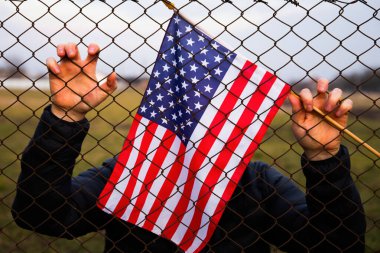 Amerikan Bayrağı 'nı ABD sınırında dikenli tellerin yanında tutan adam. Amerikan göçmenlik ve ABD mülteci krizi kavramı