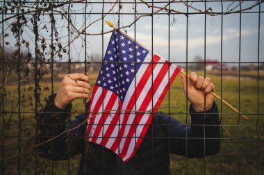 Amerikan Bayrağı 'nı ABD sınırında dikenli tellerin yanında tutan adam. Amerikan göçmenlik ve ABD mülteci krizi kavramı