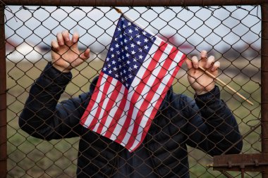 Amerikan Bayrağı 'nı ABD sınırında dikenli tellerin yanında tutan adam. Amerikan göçmenlik ve ABD mülteci krizi kavramı