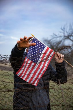 Amerikan Bayrağı 'nı ABD sınırında dikenli tellerin yanında tutan adam. Amerikan göçmenlik ve ABD mülteci krizi kavramı