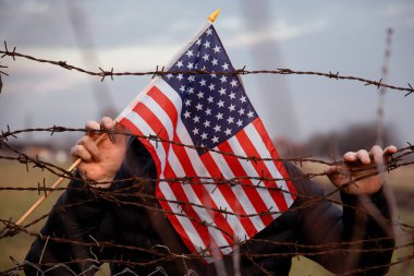 Amerikan Bayrağı 'nı ABD sınırında dikenli tellerin yanında tutan adam. Amerikan göçmenlik ve ABD mülteci krizi kavramı