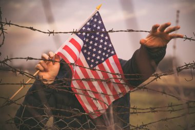 Amerikan Bayrağı 'nı ABD sınırında dikenli tellerin yanında tutan adam. Amerikan göçmenlik ve ABD mülteci krizi kavramı