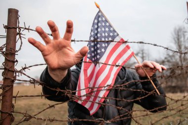 Amerikan Bayrağı 'nı ABD sınırında dikenli tellerin yanında tutan adam. Amerikan göçmenlik ve ABD mülteci krizi kavramı