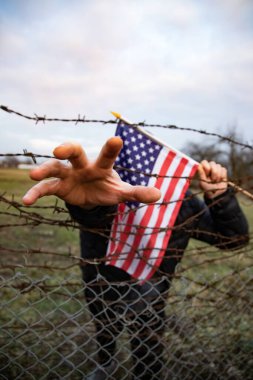 Amerikan Bayrağı 'nı ABD sınırında dikenli tellerin yanında tutan adam. Amerikan göçmenlik ve ABD mülteci krizi kavramı