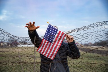 Amerikan Bayrağı 'nı ABD sınırında dikenli tellerin yanında tutan adam. Amerikan göçmenlik ve ABD mülteci krizi kavramı