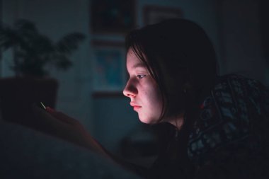 Akıllı telefon kullanan genç kız, gece geç saatte yatakta yatan tablet. Çocukların ekran bağımlılığı konsepti..