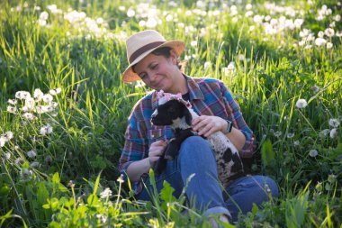 Baharda küçük şirin bir kuzuyu elinde tutan dişi çiftçi. Yeşil çimenler ve sihirli günbatımı..