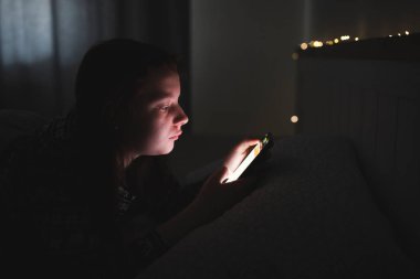 Akıllı telefon kullanan genç kız, gece geç saatte yatakta yatan tablet. Çocukların ekran bağımlılığı konsepti..