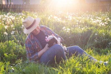Baharda küçük şirin bir kuzuyu elinde tutan dişi çiftçi. Yeşil çimenler ve sihirli günbatımı..
