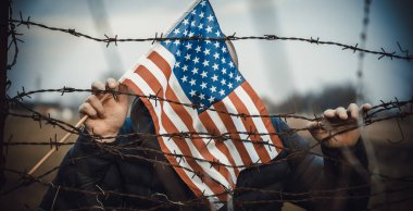 Amerikan Bayrağı 'nı ABD sınırında dikenli tellerin yanında tutan adam. Amerikan göçmenlik ve ABD mülteci krizi kavramı