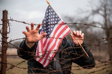 Amerikan Bayrağı 'nı ABD sınırında dikenli tellerin yanında tutan adam. Amerikan göçmenlik ve ABD mülteci krizi kavramı