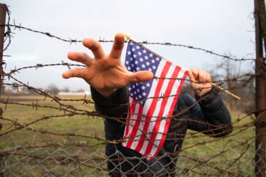 Amerikan Bayrağı 'nı ABD sınırında dikenli tellerin yanında tutan adam. Amerikan göçmenlik ve ABD mülteci krizi kavramı