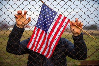Amerikan Bayrağı 'nı ABD sınırında dikenli tellerin yanında tutan adam. Amerikan göçmenlik ve ABD mülteci krizi kavramı