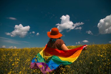 Çayırda LGTB bayrağı sallayan ikili olmayan kişi. LGBT gurur kavramı