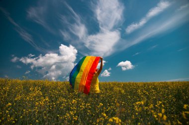 Çayırda LGTB bayrağı sallayan ikili olmayan kişi. LGBT gurur kavramı.