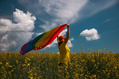 Çayırda LGTB bayrağı sallayan ikili olmayan kişi. LGBT gurur kavramı.