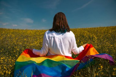 Çayırda LGTB bayrağı sallayan ikili olmayan kişi. LGBT gurur kavramı.