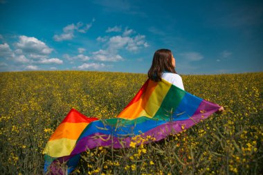 Çayırda LGTB bayrağı sallayan ikili olmayan kişi. LGBT gurur kavramı.