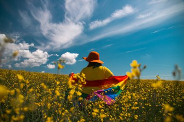 Çayırda LGTB bayrağı sallayan ikili olmayan kişi. LGBT gurur kavramı.