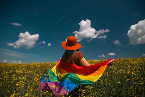 Çayırda LGTB bayrağı sallayan ikili olmayan kişi. LGBT gurur kavramı