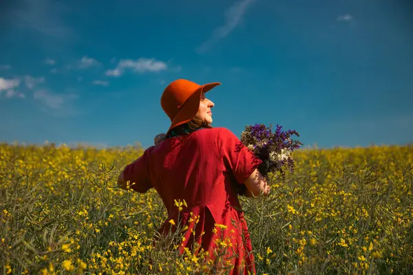 Güzel bir kadın elinde bir buket yaban çiçeği tutuyor, muhteşem doğanın tadını çıkarıyor. Yaz yaşam tarzı konsepti.